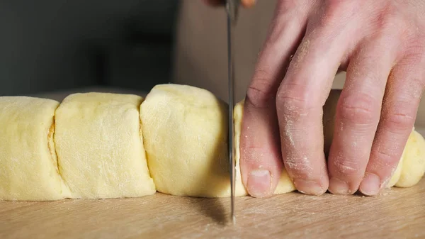 Шеф-повар пекаря нарезает булочки с корицей, сахаром и маслом на порциях, чтобы печь булочки с корицей . — стоковое фото