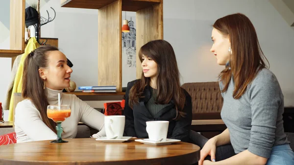 Drei Freundinnen in einem Café unterhalten sich und trinken ihre Getränke. — Stockfoto