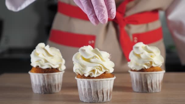Pastelero espolvorea magdalenas con crema en tazas de papel con miga de chocolate . — Vídeos de Stock
