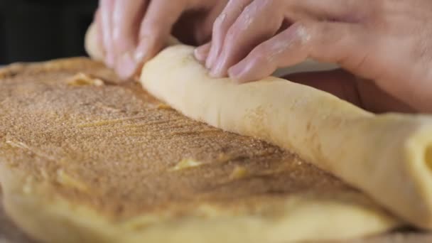 Bäckermeister rollt den Teig mit Zimt, Zucker und Butter zu einer Rolle auf dem Tisch. — Stockvideo