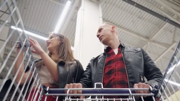 Jong paar koopt producten in een supermarkt en zet ze in een trolley. — Stockvideo