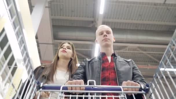 Νεαρό ζευγάρι αγοράζει προϊόντα σε ένα σούπερ μάρκετ και τα βάζει σε ένα τρόλεϊ. — Αρχείο Βίντεο