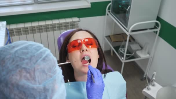 Ung flicka i skyddsglasögon på förebyggande undersökning i tandläkarmottagningen. Tandvård koncept. — Stockvideo