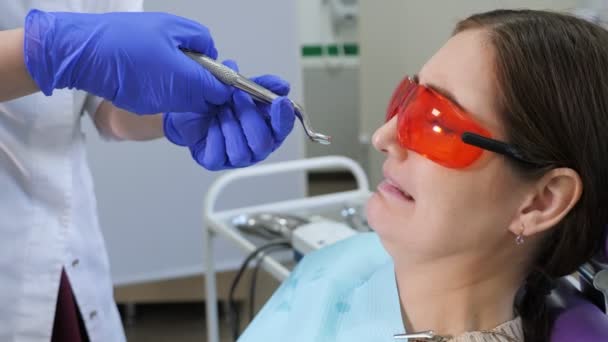 Mujer joven con miedo de quitarse un diente sentado en la silla dental mientras el médico está de pie junto al paciente, sosteniendo fórceps en las manos . — Vídeo de stock
