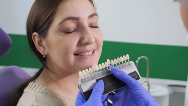 Dentista com amostras de cor de dente está escolhendo sombra para mulheres dentes de paciente na clínica odontológica . — Vídeo de Stock