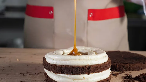 Pastelero está vertiendo caramelo en pastel de esponja de chocolate. Hacer pastel en panadería . —  Fotos de Stock