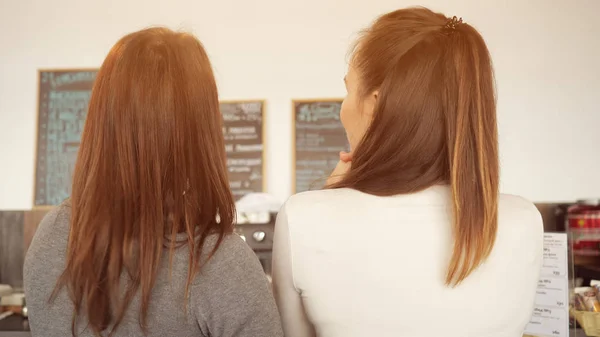 Dos mujeres discuten el menú y eligen la comida en un café de pie en el mostrador del bar . — Foto de Stock