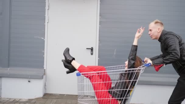 Mann rollt seine attraktive junge Freundin in den Einkaufswagen auf dem Parkplatz des Supermarktes. — Stockvideo
