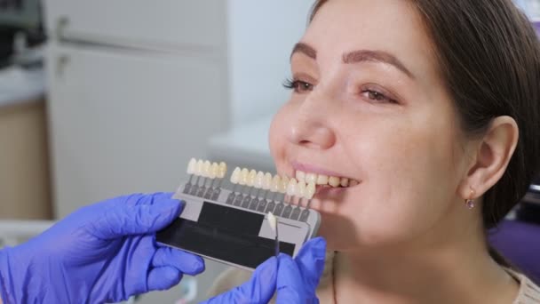 Dentista com amostras de cor de dente está escolhendo sombra para mulheres dentes de paciente na clínica odontológica . — Vídeo de Stock