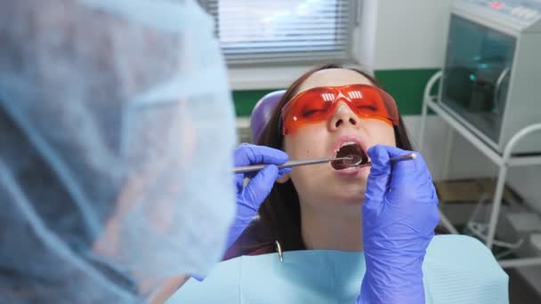 在牙科诊所，戴防护眼镜的小女孩在牙科椅子上接受预防性检查。 牙齿护理概念. — 图库视频影像