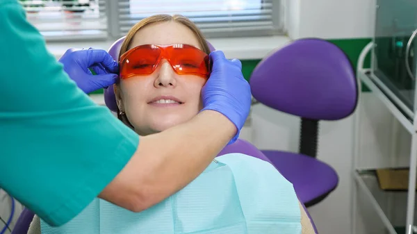 Zahnarzt setzt der Patientin, die vor der Untersuchung im Zahnarztstuhl sitzt, eine Brille auf. — Stockfoto