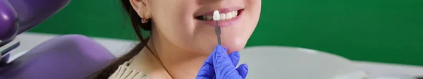 歯の色のサンプルが付いている歯科医は歯科医院の女性の患者の歯のための色合いを選ぶ. — ストック写真