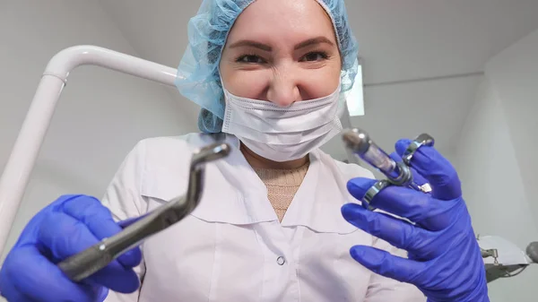Diş hekimi kadın doktor elinde diş aletleri forseps ve iğne tutuyor ve kamera bakıyor. — Stok fotoğraf