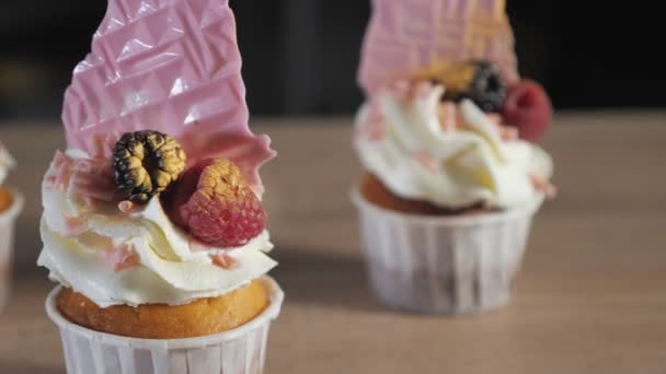 Cupcakes con crema, gofres y bayas frescas en vasos de papel sobre la mesa . — Vídeo de stock