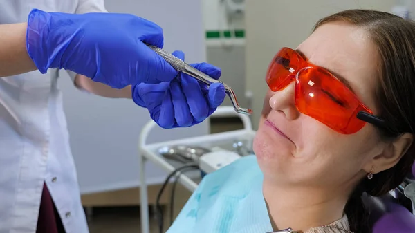 Jonge vrouw bang om een tand zittend in tandartsstoel te verwijderen terwijl de arts naast de patiënt staat, met een tang in de hand. — Stockfoto