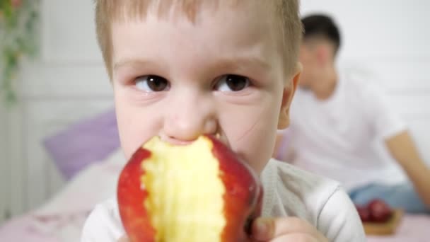 Küçük çocuk ebeveynlerin yatak odasında elma yiyor. Ailesi arka planda yatakta oturuyor.. — Stok video