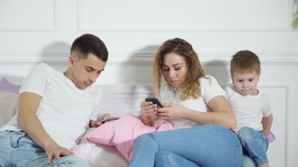 Родители смотрят в свои мобильные телефоны, не обращая внимания на своего ребенка. Побег из реальности, зависимость от гаджетов . — стоковое видео