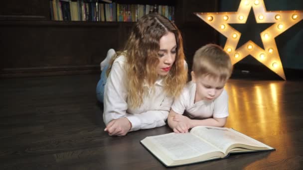 Porträtt av ung kvinna läser en bok med sin lille son. — Stockvideo