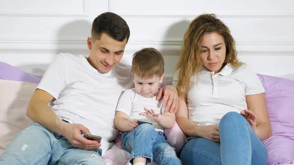 Family with child are looking in their mobile phones laying on the bed. Dependence from gadgets.