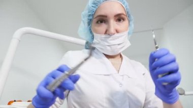 Diş hekimi kadın doktor elinde diş aletleri forseps ve iğne tutuyor ve kamera bakıyor.