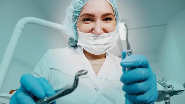 Zahnärztin hält Pinzette und Nadel in der Hand und blickt in die Kamera. — Stockfoto