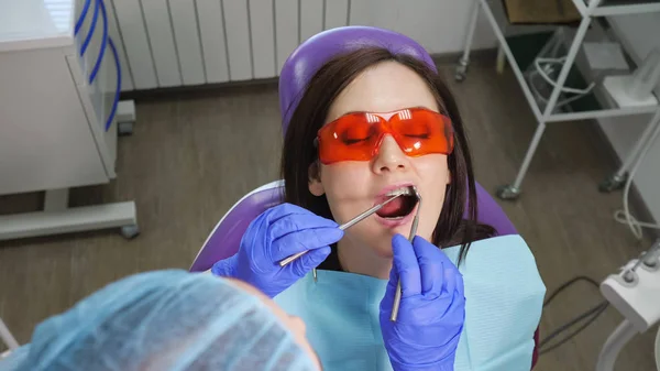 Jong meisje in beschermende bril op preventief onderzoek in tandartsstoel in de tandartsenkliniek. Tandverzorging concept. — Stockfoto
