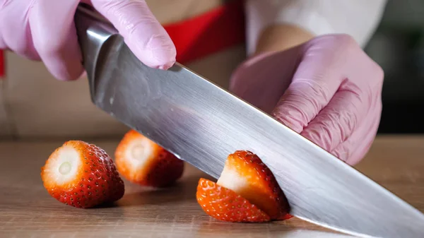 Chef is cutting strawberry on slices in rubber gloves on wooden table. — Stock Photo, Image