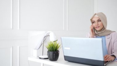 Çekici rahat Müslüman kadın onun işyerinde oturan cep telefonu konuşuyor.