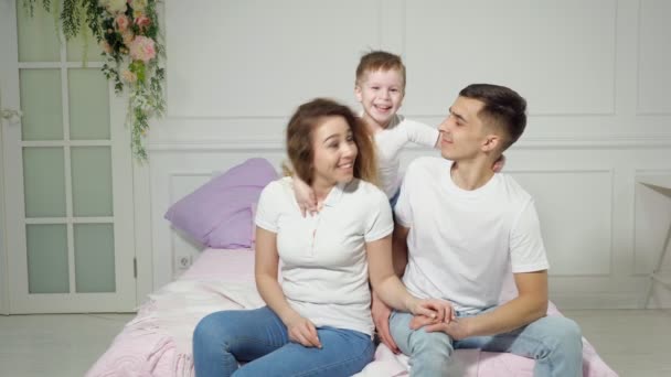 Niño pequeño está abrazando a sus padres sentados en la cama . — Vídeos de Stock