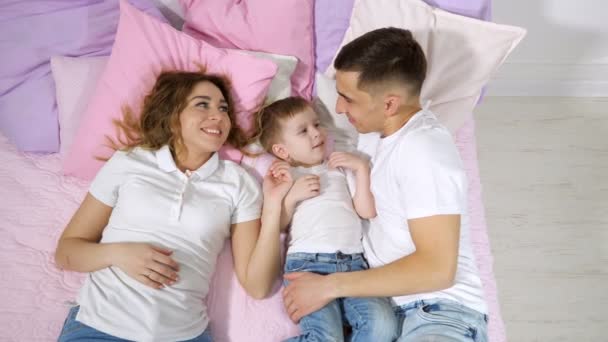 Familia feliz en la cama, mamá, hijo y papá se besan y abrazan juntos . — Vídeos de Stock