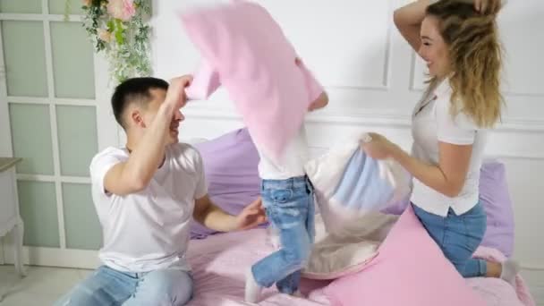 Familia joven: mamá papá y su hijo pequeño se divierten pelea de almohadas en la cama . — Vídeos de Stock