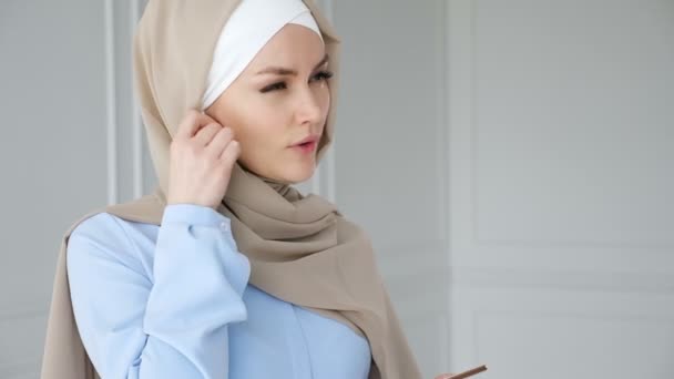 Donna musulmana che indossa hijab sta parlando smartphone con auricolare wireless . — Video Stock