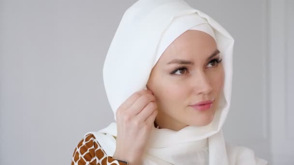 Mulher muçulmana vestindo hijab está colocando fone de ouvido sem fio em seu ouvido e telefone falando usando fone de ouvido . — Vídeo de Stock