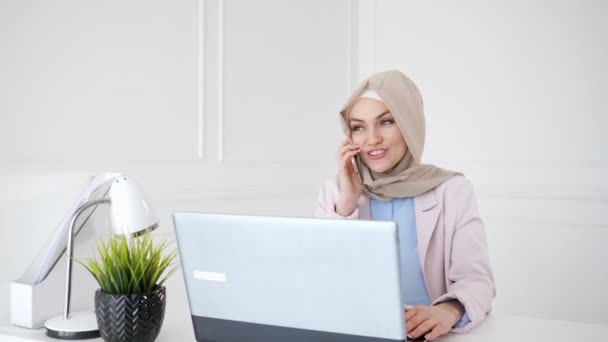 Belle femme musulmane détendue parle téléphone mobile assis sur son lieu de travail . — Video