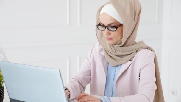 Nörd Muslim kvinna i hijab arbetar på en examen kandidatprojekt skriva på laptop och titta på SmartWatch. — Stockvideo