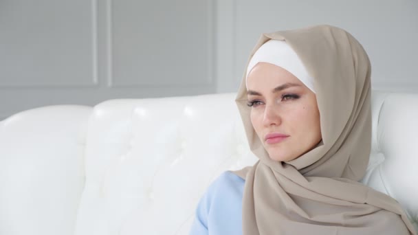 Θλιβερό κλάμα μουσουλμανική γυναίκα στη μαντίλα είναι κάθεται στον καναπέ στο σπίτι. — Αρχείο Βίντεο