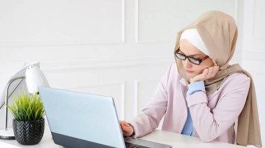 Başörtüsü ve gözlüklü kadın dizüstü bilgisayarıyla sıkıcı işler yapıyor..