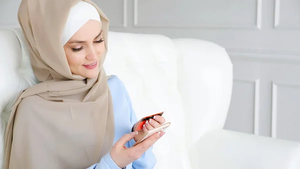 Muslim kvinna i hijab köper online med ett kreditkort och smartphone. — Stockfoto