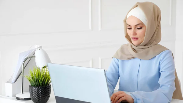 Νεαρή μουσουλμάνα δακτυλογραφεί σε φορητό υπολογιστή που εργάζεται στο γραφείο. — Φωτογραφία Αρχείου