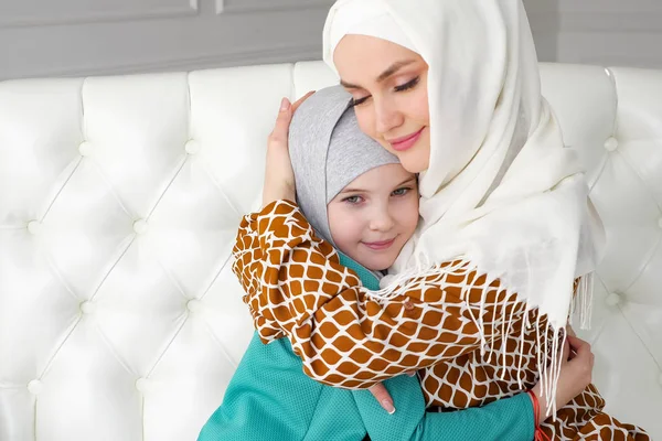 Muslim mamma och hennes lilla dotter i hijab är kramar sitter på soffan. — Stockfoto