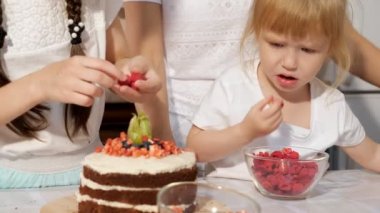 Aile, iki küçük kızları ile anne evde mutfakta birlikte çilek ile Doğum günü pastası dekorasyon.
