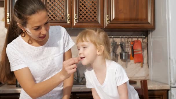 Mãe alimenta sua filha um pedaço de chocolate na cozinha . — Vídeo de Stock