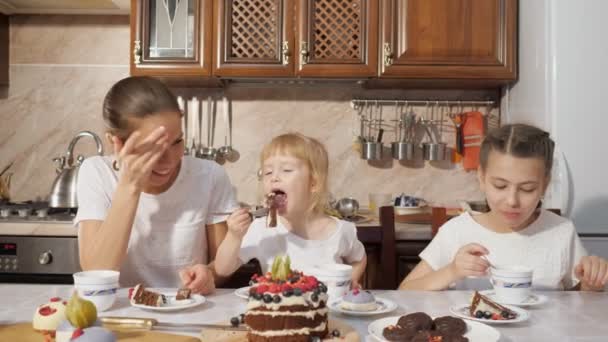 Mamma och två döttrar har en te med hemlagad choklad kaka i köket, familjens födelsedag hemma. — Stockvideo