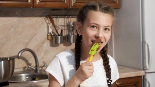 Adolescent fille lèche plastique spatule avec chocolat et sourire . — Video