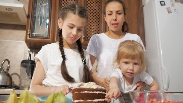Família, mãe com duas filhas pequenas estão decorando bolo de aniversário com bagas juntas na cozinha em casa . — Vídeo de Stock