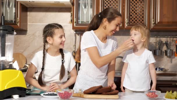 Mutter füttert ihre Tochter in der Küche mit einem Stück Schokolade. — Stockvideo