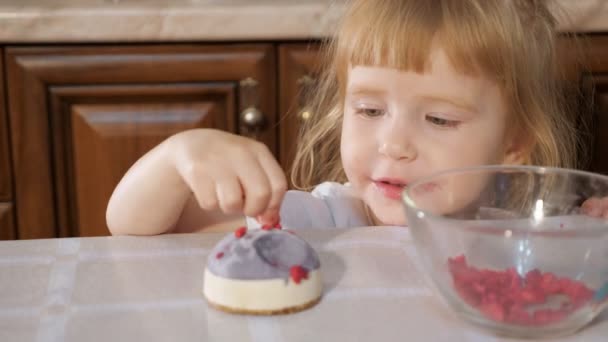 Pequeña linda chica está decorando pequeño pastel con frambuesa . — Vídeos de Stock