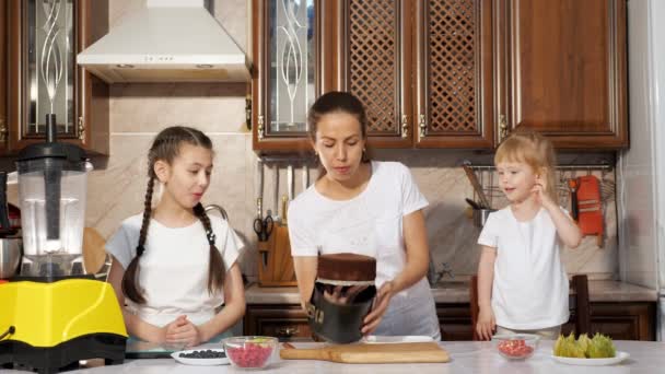 Mãe está fazendo um bolo com suas duas filhas pequenas na cozinha . — Vídeo de Stock