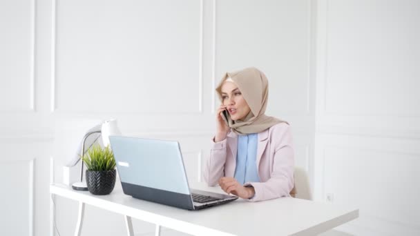 Belle femme musulmane détendue parle téléphone mobile assis sur son lieu de travail . — Video