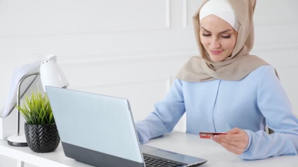 Moslim vrouw in hijab is online kopen met een creditcard en laptop. — Stockvideo